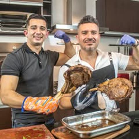 Nene Chávez y un colega en una cocina, con guantes de horno, sosteniendo un tomahawk y una pierna de cerdo recién salidos del horno